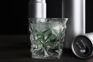 Photo of Energy drink in glass and aluminium cans on wooden table, closeup