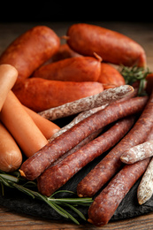 Different tasty sausages on wooden table, closeup