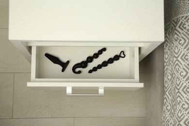 Photo of Black anal plug and beads in open drawer of bedside table indoors, above view. Sex toys