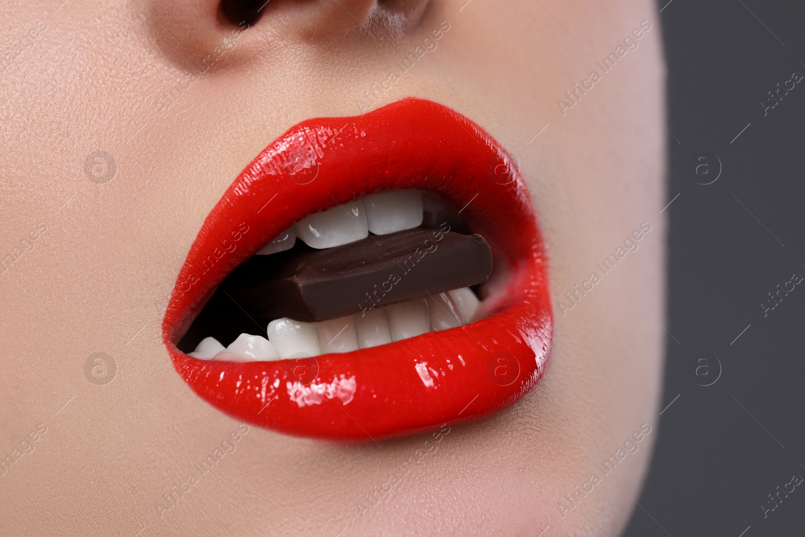 Photo of Young woman with beautiful lips eating chocolate on grey background, closeup