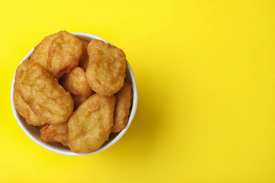 Photo of Bucket with tasty chicken nuggets on yellow background, top view. Space for text