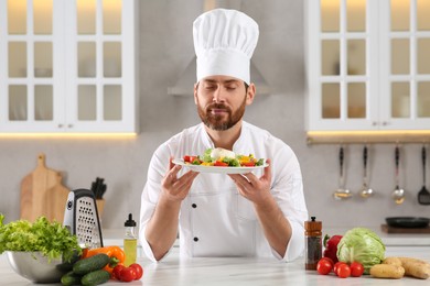 Photo of Professional chef smelling delicious salad at marble table in kitchen
