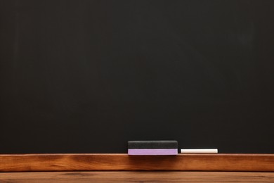 Piece of chalk and duster on wooden table near blackboard, space for text