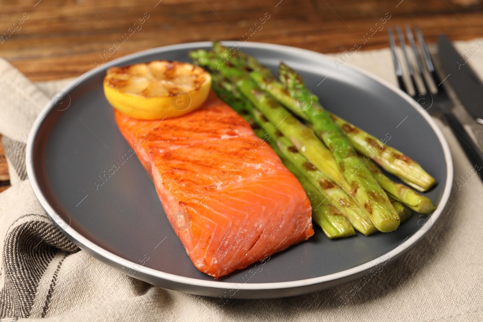 Photo of Tasty grilled salmon with asparagus and lemon served on table, closeup