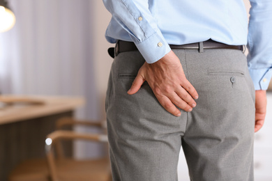 Photo of Man suffering from hemorrhoid in office, closeup