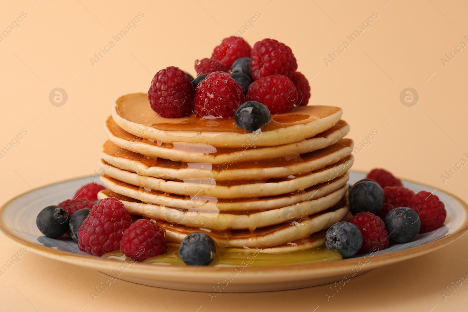 Photo of Stack of tasty pancakes with raspberries, blueberries and honey on pale orange background, closeup