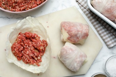 Photo of Preparing stuffed cabbage rolls on white marble table, flat lay