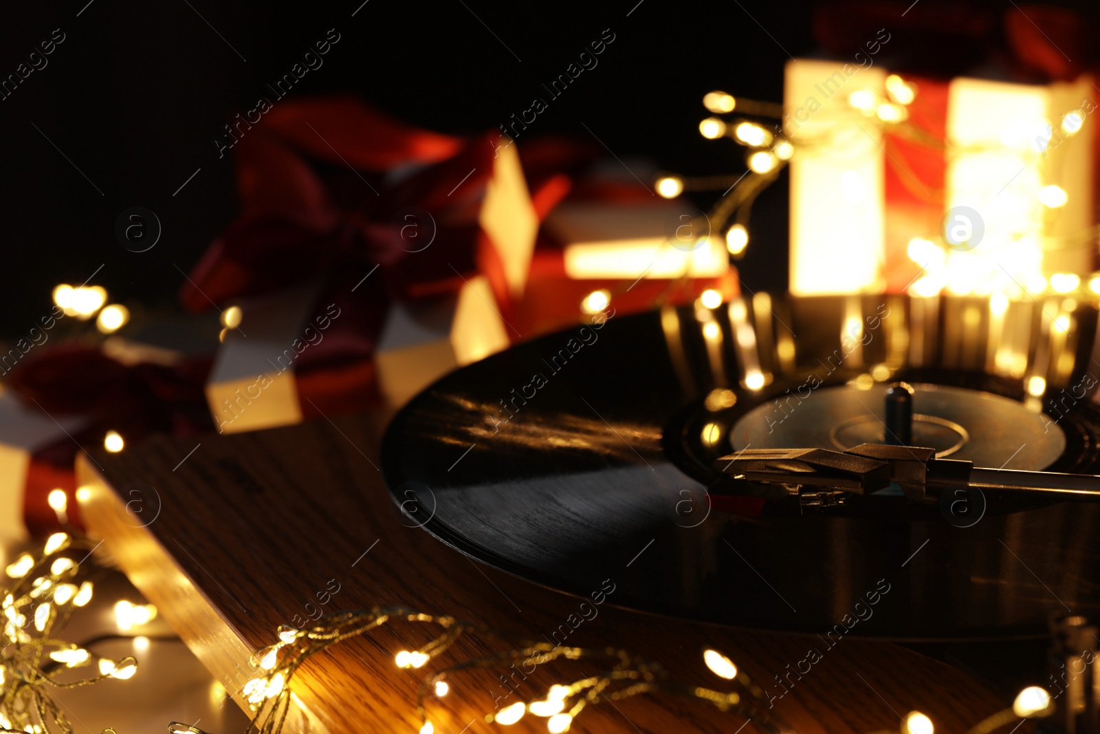 Photo of Turntable with vinyl record, fairy lights and Christmas gift boxes, closeup