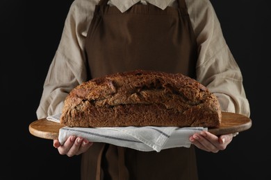 Photo of Woman holding freshly baked bread on black background, closeup