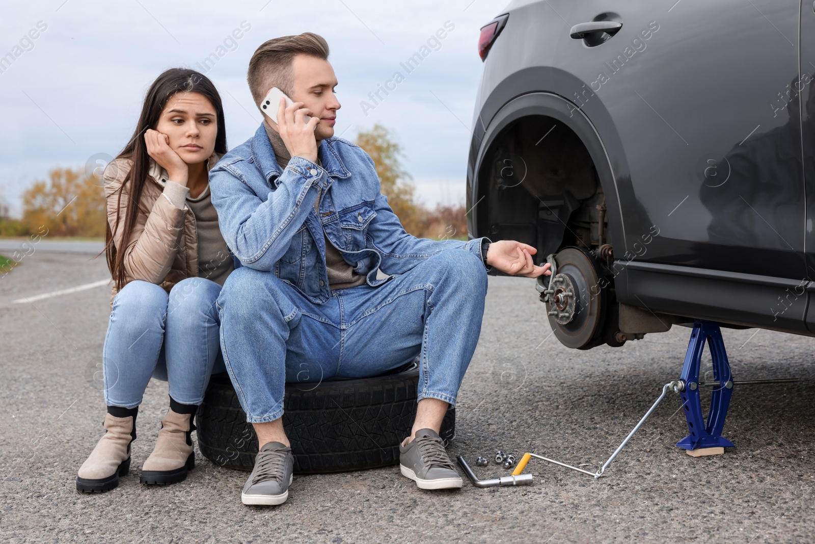 Photo of Young man calling to car service on roadside. Tire puncture