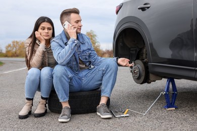 Photo of Young man calling to car service on roadside. Tire puncture