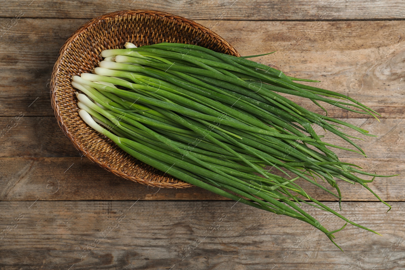 Photo of Wicker bowl with green onions on wooden table, top view