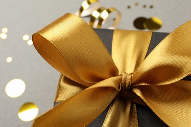 Beautiful black gift box with golden bow on grey background, closeup