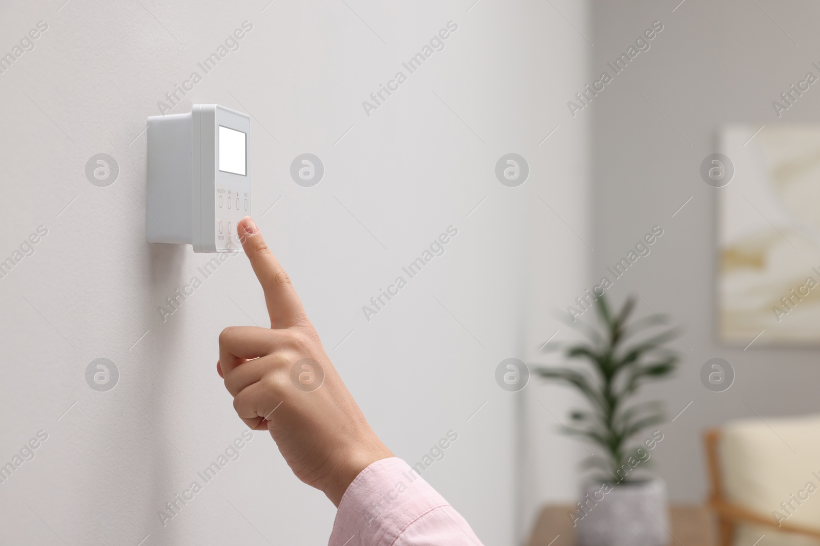 Photo of Woman adjusting thermostat on white wall indoors, closeup and space for text. Smart home system