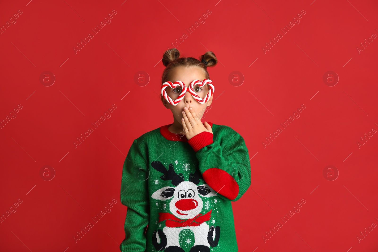 Photo of Surprised little girl in Christmas sweater and party glasses on red background