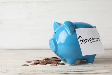 Photo of Piggy bank with word PENSION and coins on table. Space for text