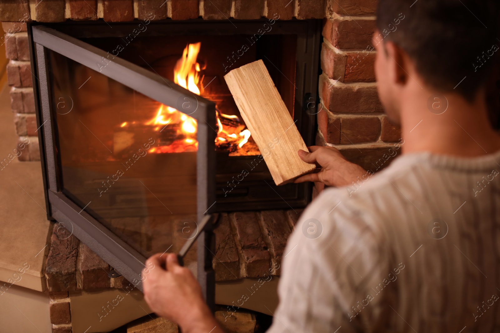 Photo of Man putting dry firewood into fireplace at home, closeup. Winter vacation