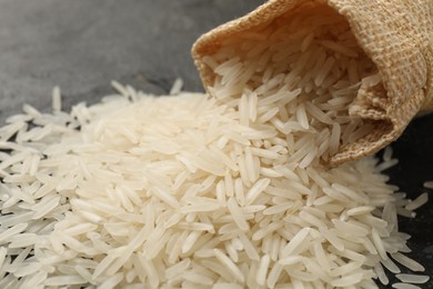 Photo of Raw basmati rice and overturned sack on table, closeup