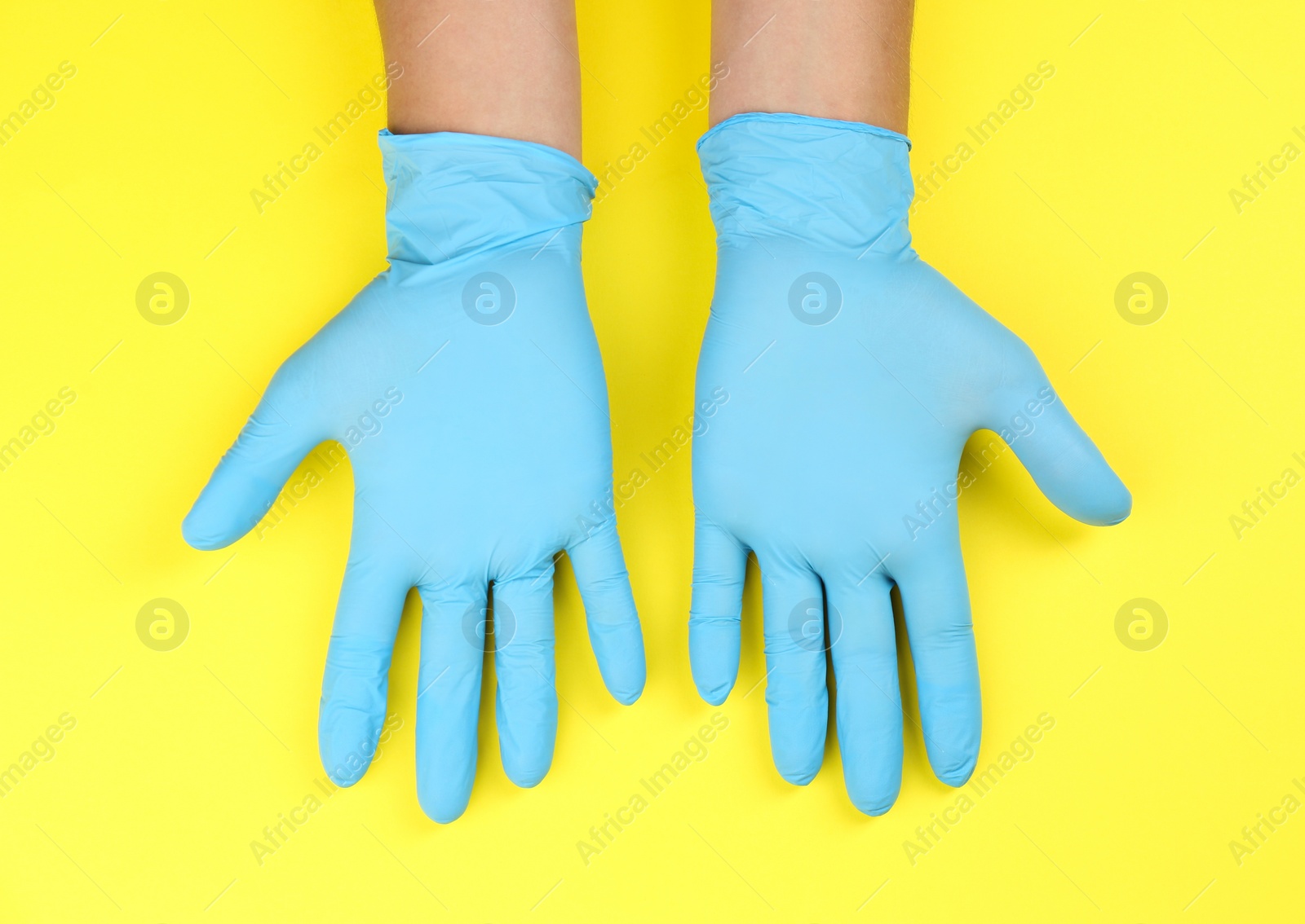 Photo of Person in blue latex gloves against yellow background, closeup on hands