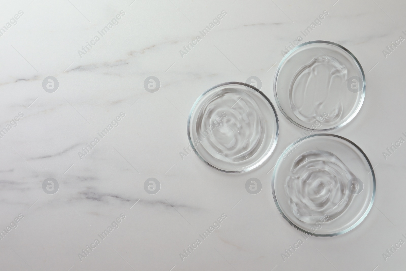 Photo of Petri dishes with liquids on white marble table, flat lay. Space for text