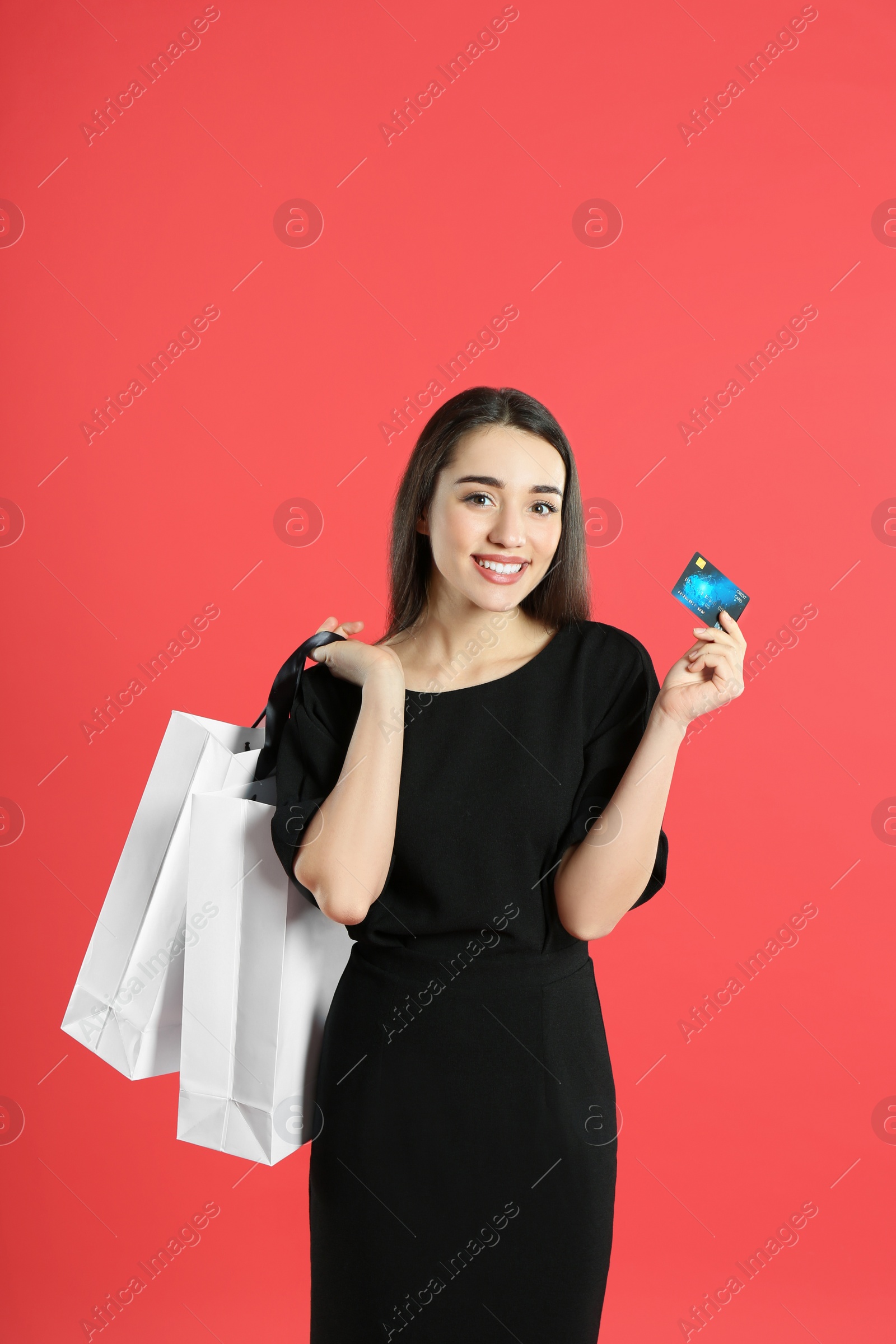 Photo of Young woman with credit card and shopping bags on crimson background. Spending money