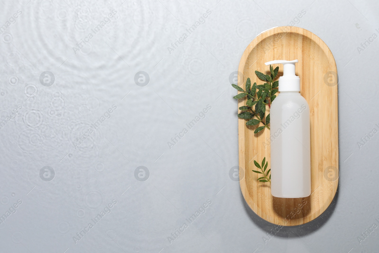 Photo of Wooden tray with bottle of facial cleanser and leaves in water on light grey background, top view. Space for text