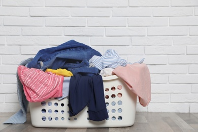 Photo of Laundry basket with dirty clothes on floor near brick wall. Space for text