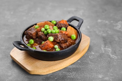Photo of Delicious beef stew with carrots, peas and potatoes on grey table, closeup. Space for text