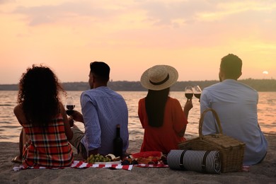 Group of friends having picnic near river at sunset, back view