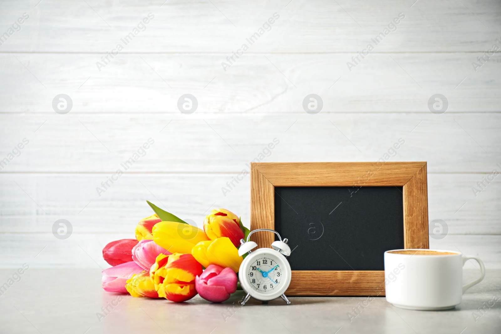 Photo of Chalkboard with morning wish, delicious coffee, tulips and alarm clock on light grey table