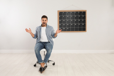 Photo of Young man sitting near board calendar indoors