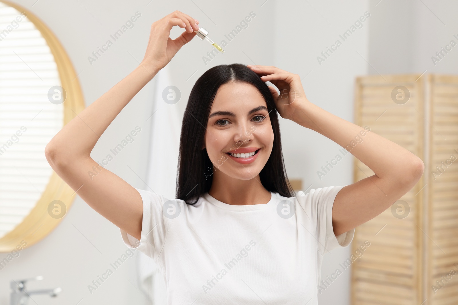 Photo of Beautiful woman applying hair serum in bathroom. Cosmetic product