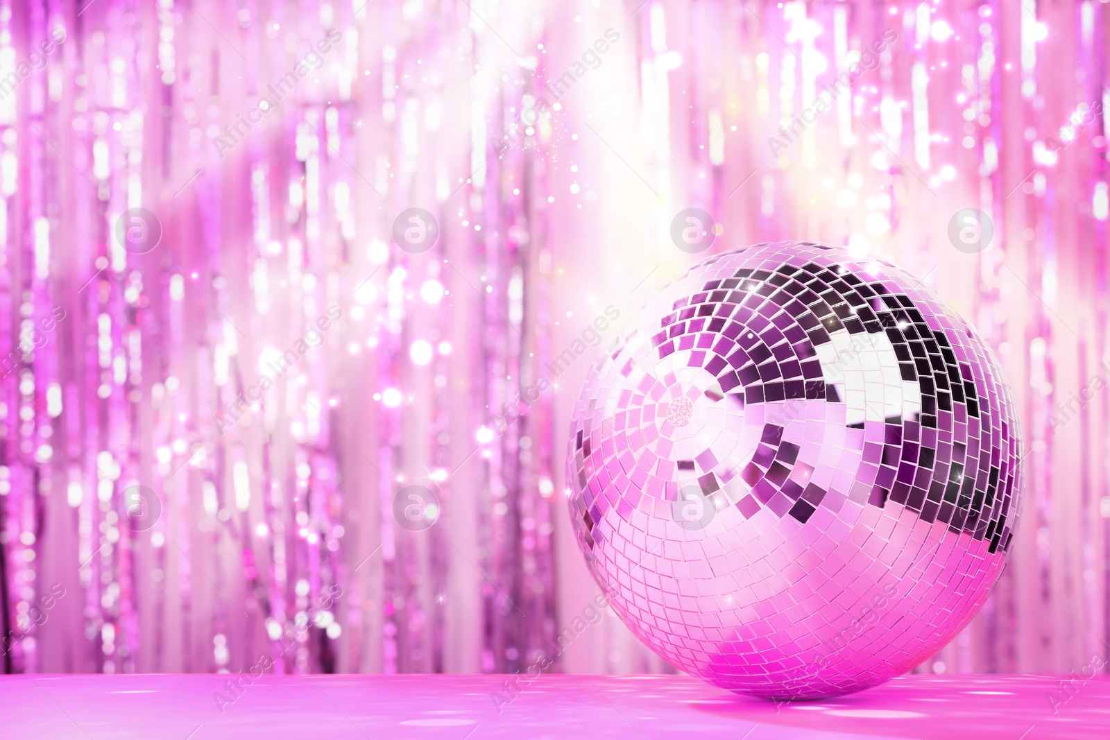 Image of Shiny disco ball on table against foil party curtain, space for text. Bokeh effect