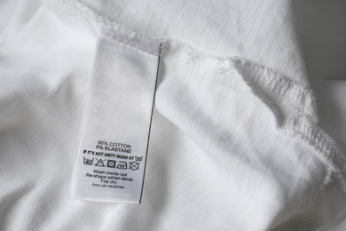 Photo of Clothing label with care symbols and material content on white shirt, closeup view