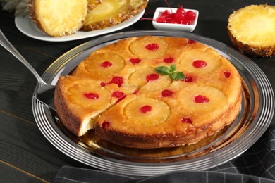 Photo of Taking piece of delicious cut pineapple pie with cherry and mint on dark wooden table