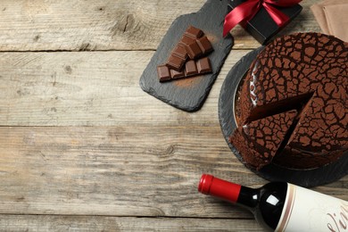 Photo of Delicious truffle cake, bottle of wine, chocolate pieces and gift box on wooden table, flat lay. Space for text