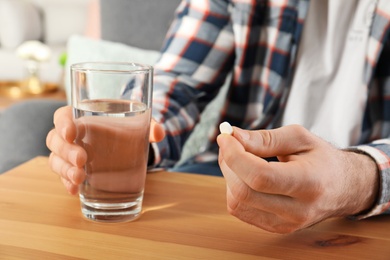 Photo of Man holding pill and glass of water at table, closeup