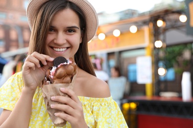 Pretty young woman holding delicious sweet bubble waffle with ice cream outdoors