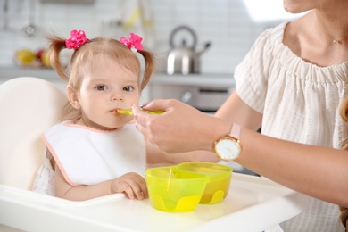 Photo of Mother feeding her little baby with healthy food in kitchen