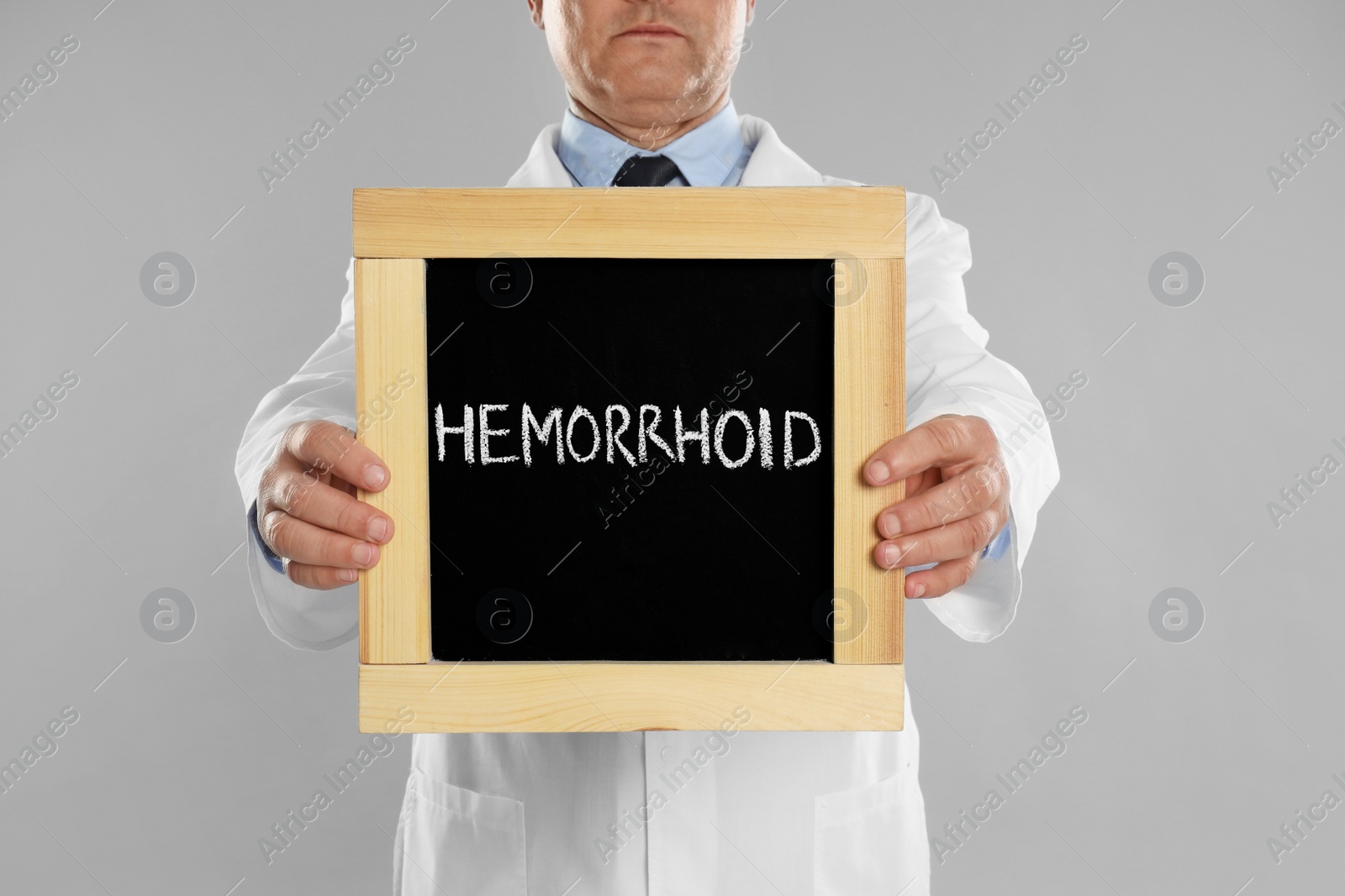 Photo of Doctor holding blackboard with word HEMORRHOID on light grey background, closeup