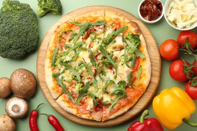 Photo of Delicious vegetarian pizza and products on green table, flat lay