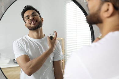 Man spraying luxury perfume near mirror indoors