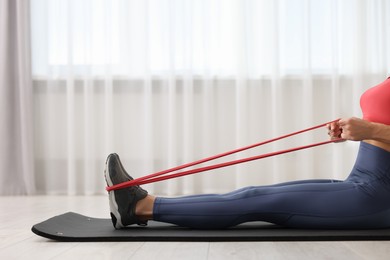 Woman doing exercise with fitness elastic band on mat indoors, closeup