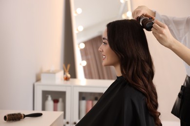 Photo of Hairdresser working with beautiful woman using curling hair iron in salon. Space for text