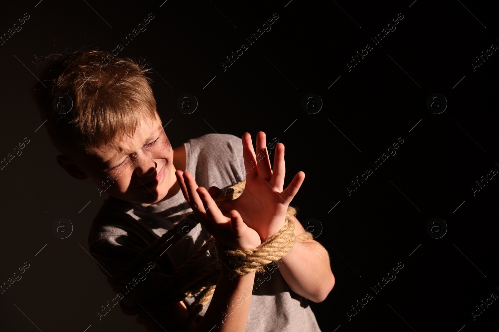 Photo of Scarred little boy with bruises tied up and taken hostage on dark background. Space for text