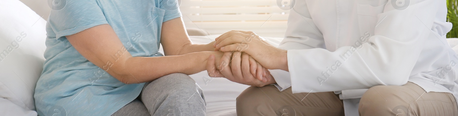 Image of Doctor and senior patient holding hands in hospital, closeup. Banner design