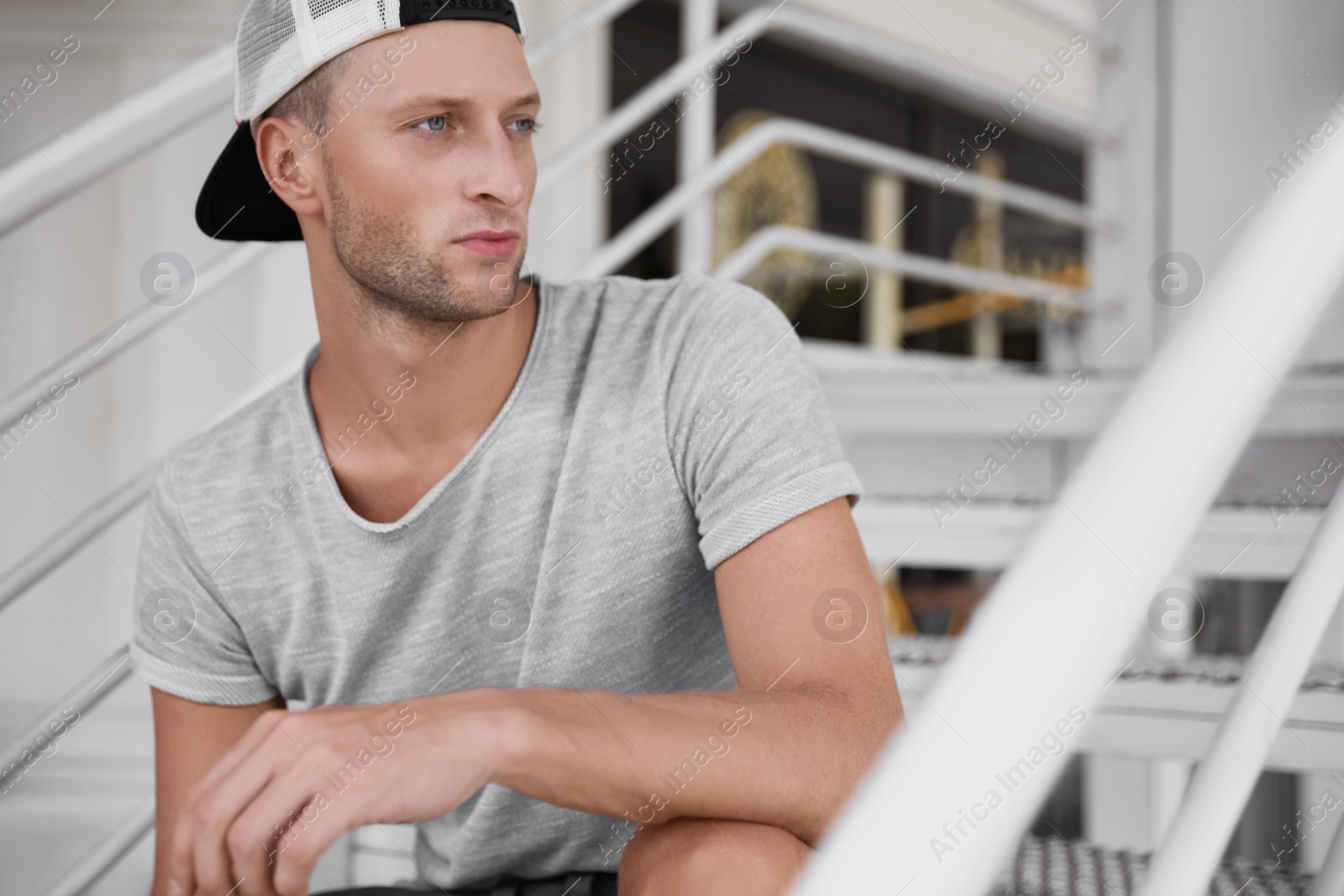 Photo of Handsome young man in stylish cap sitting on stairs outdoors