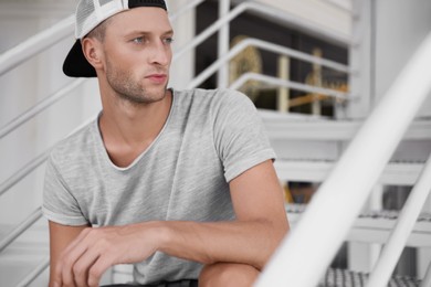 Photo of Handsome young man in stylish cap sitting on stairs outdoors
