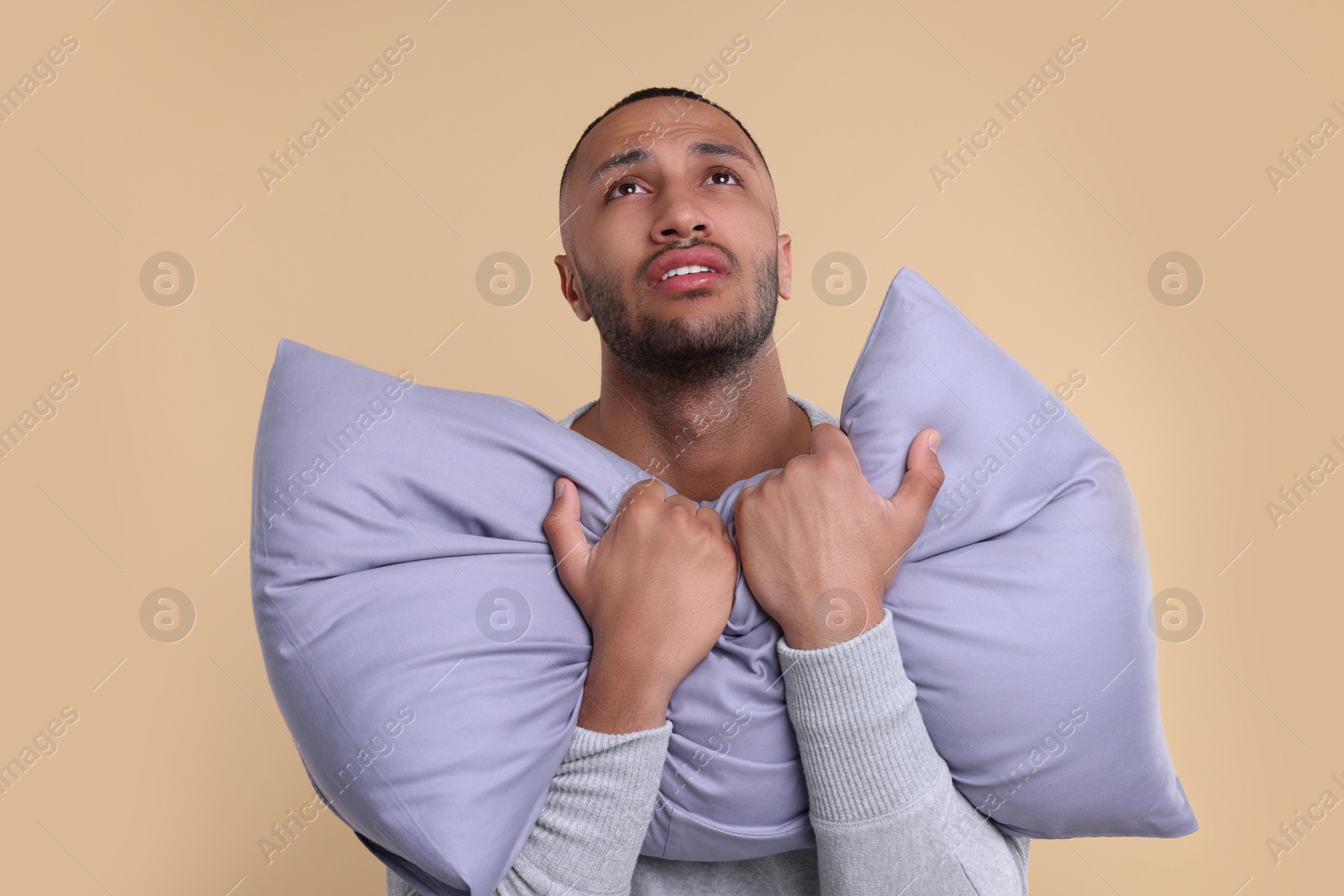 Photo of Unhappy man with pillow on beige background. Insomnia problem