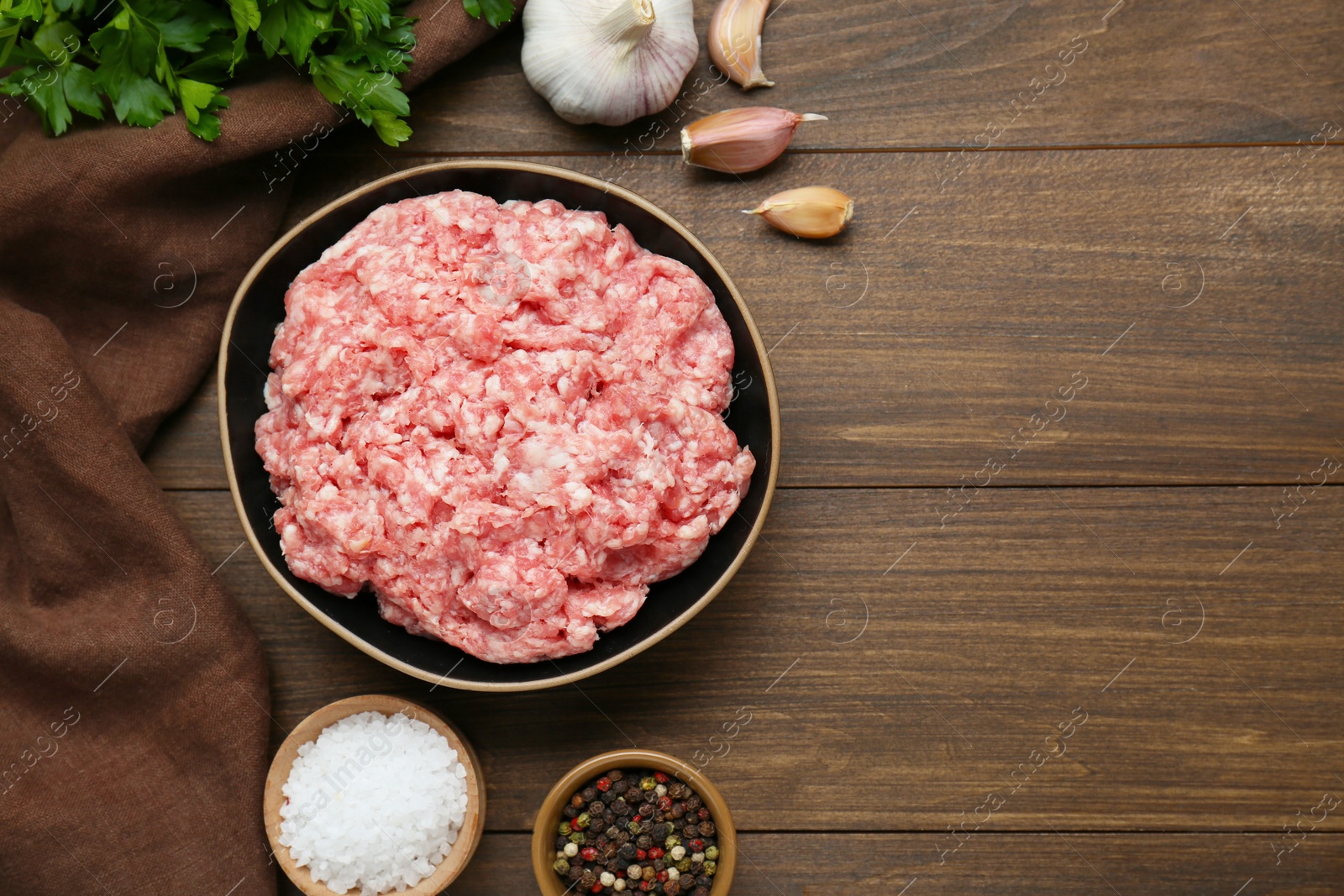 Photo of Bowl of raw fresh minced meat and ingredients on wooden table, flat lay. Space for text